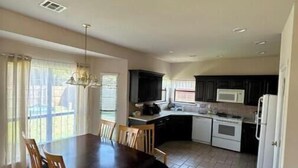 Une cuisine spacieuse avec des meubles de couleur sombre, un réfrigérateur blanc et un coin repas comprenant une table et des chaises en bois.