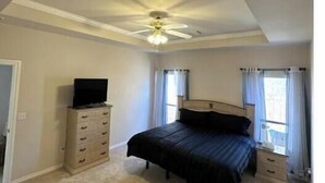 Une chambre à coucher comprenant un lit, une commode, un téléviseur et un ventilateur de plafond.