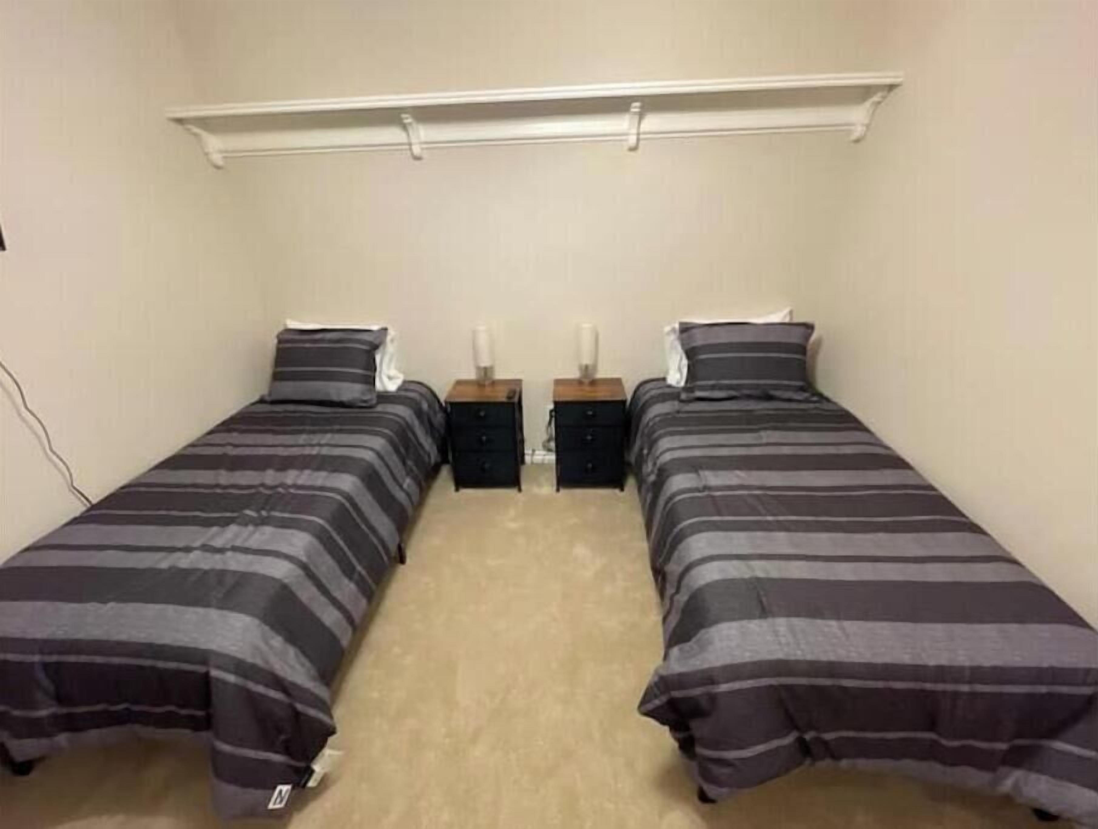 Une petite chambre propre, avec deux lits simples, chacun agrémenté d’un oreiller assorti et d’une table de chevet.