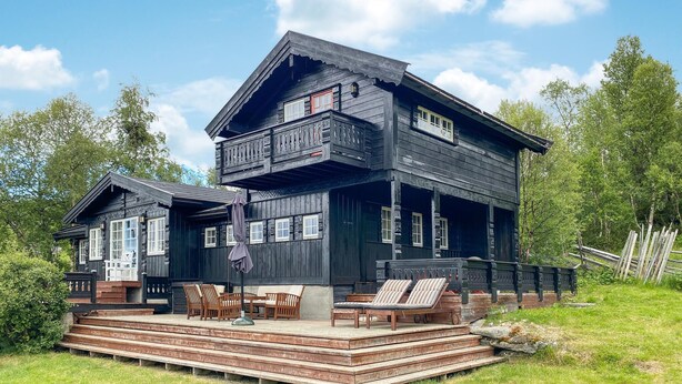 A two-story wooden house with a balcony, outdoor seating, and a deck.