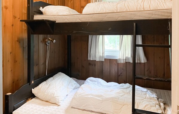 A bunk bed with a headboard, a small window with curtains, and a wooden wall.