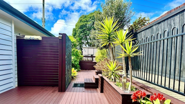 A wooden deck with a dark gate, a metal fence, and various plants.