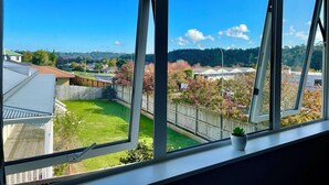 A view from a window with a clear sky, a green lawn, a wooden fence, and a distant hill.