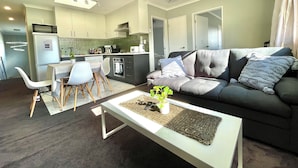 A modern living room with a grey sofa, white coffee table, and a dining area with a white table and chairs.