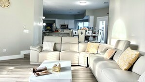 Un salon moderne avec un canapé d’angle beige, une table basse blanche et une cuisine en arrière-plan.