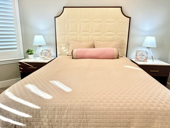 Una cama bien hecha con una colcha estampada y un cabecero decorativo. Hay dos mesitas de noche con lámparas y adornos.