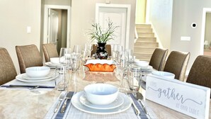 Une table à manger dressée pour un repas, avec des chaises, un centre de table et un panneau indiquant : « Venez vous réunir autour de notre table ».
