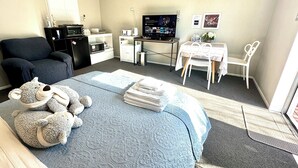 Een kleine hotelkamer met een bed, een bureau, een stoel, een televisie, een magnetron en een koelkast.