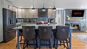 A modern kitchen with a central island, bar stools, a flat-screen TV, and a fireplace. - 5-Bedroom · Rooftop · Game Room · Sleeps 11 · Lake View (Seattle)