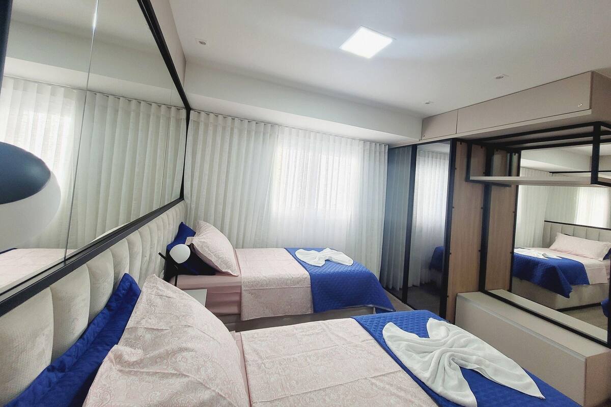 Une chambre d’hôtel avec deux lits, un grand miroir et une fenêtre avec des stores.
