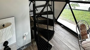 Een modern interieur met een zwarte metalen trap, houten balken en uitzicht op een auto en groen buiten.