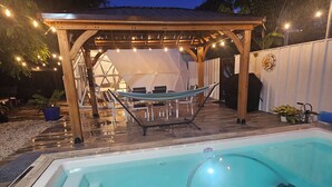 Een zwembadgedeelte met een houten pergola, een hangmat en ligbedden.