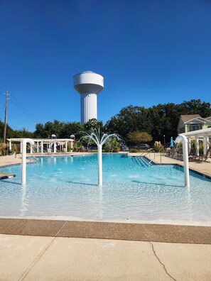 Ein Swimmingpool mit einer Springbrunnenanlage, einem hohen Wasserturm und einem Pavillon im Hintergrund.