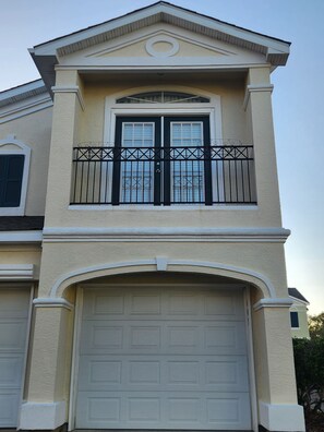 A two-story house with a white garage door, a balcony with black railings, and a decorative window above the door.