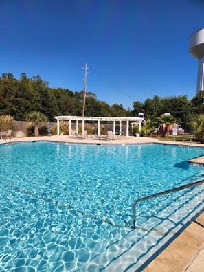 Una piscina azul cristalina con una pérgola y sillones de descanso al fondo.