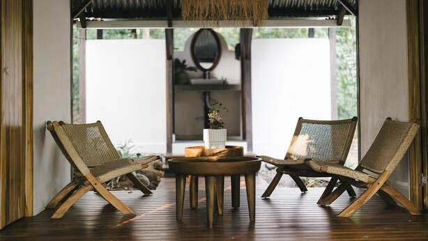 A room with two wicker chairs, a round wooden table, and a hanging light fixture.
