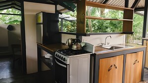 A compact kitchen with a gas stove, kettle, sink, and wooden cabinets.