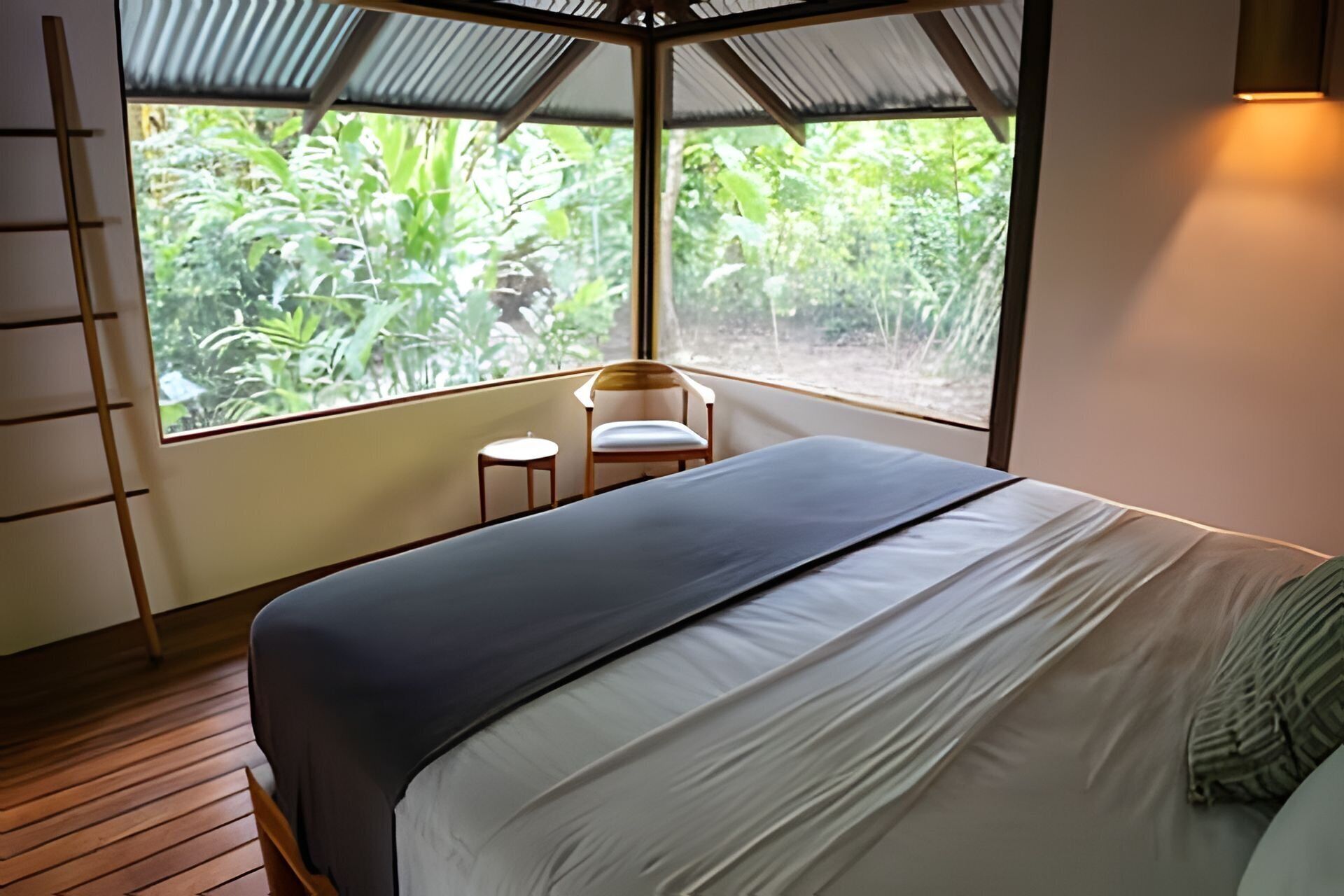 A bedroom with a bed, a chair, and a window overlooking greenery.