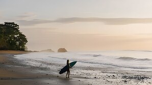 A beach with a person carrying a surfboard, waves, and distant landforms.