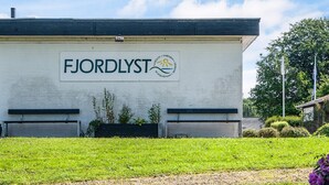 A building with a sign that reads "FJORDLYST" and a logo with a sun and waves. - Lush Cabin in Camping Resort (Aabenraa)