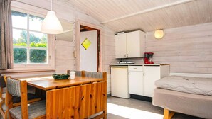 A cozy room with a wooden dining table, a sofa, a kitchenette, and a window with curtains. - Lush Cabin in Camping Resort (Aabenraa)