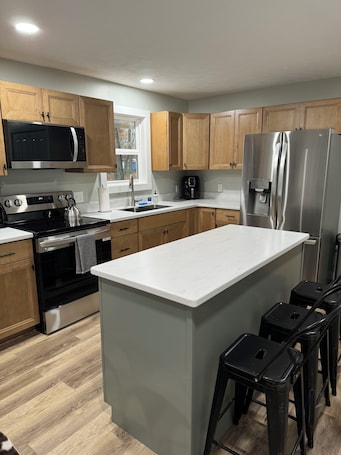 A modern kitchen with wooden cabinets, stainless steel appliances, a central island, and bar stools.