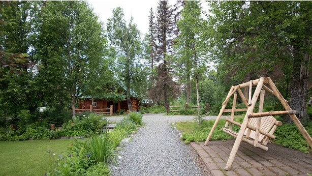 A rustic wooden swing set in a forested garden area with a gravel path leading to a wooden cabin. - The Moose Nugget Cabin (Trapper Creek)