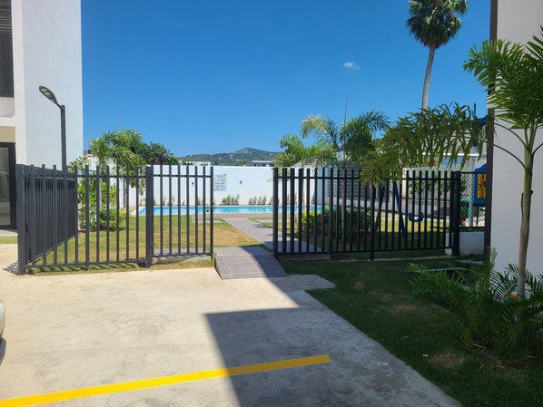 A gated entrance to a property with a pool, surrounded by greenery and a clear sky. - Bello con piscina (Santiago de los Caballeros)