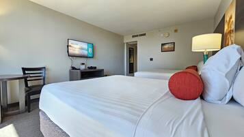 A hotel room with a bed, a desk, a chair, a television, and a lamp.