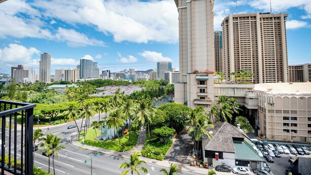 Een hoog hotel met uitzicht op een stadshemelbeeld, palmbomen en een parkeerplaats.