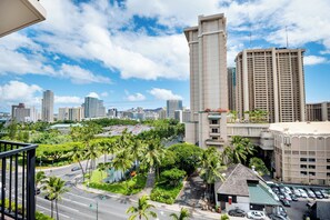 A high-rise hotel with a view of a city skyline, palm trees, and a parking area. - Palms at Waikiki by Tropical Escapes (Honolulu)