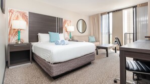 Een hotelkamer met een groot bed, een bureau, een stoel, een klein tafeltje en een spiegel.