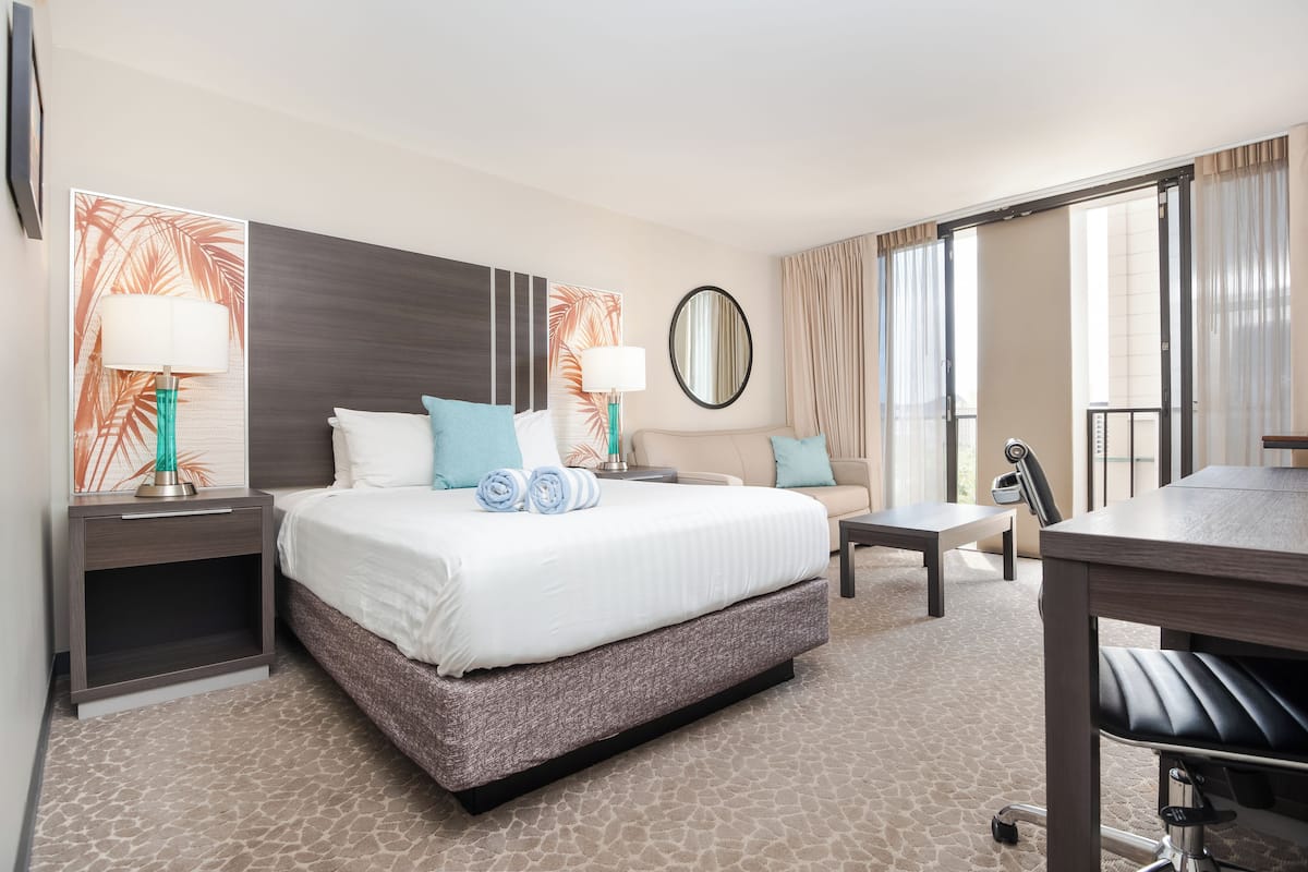 Quarto de hotel com uma cama grande, uma escrivaninha, uma cadeira, uma mesinha e um espelho.