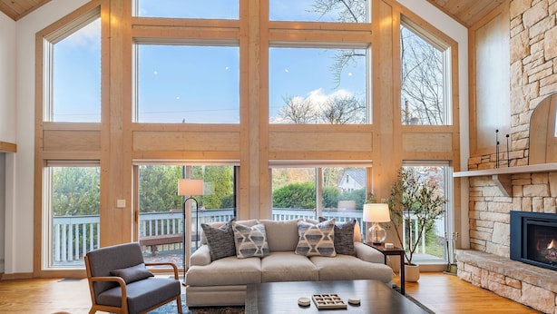 A spacious living room with a high ceiling, large windows, a fireplace, and a cozy seating area. - Lakeside Escape – Beach Access, Heated Pool, Hot Tub & Sunset Views (Lakeside)
