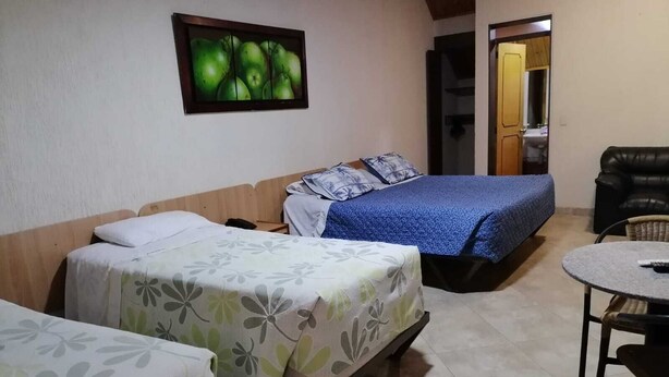 A room with two beds, a small table, and a couch. There is a painting on the wall and a door leading to another room. - Hotel Casa Colonial  (Bogotá)