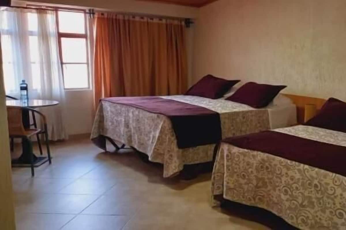 A hotel room with two beds, a small table, and a chair.