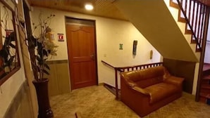 A hallway with a wooden door, a brown leather sofa, and a staircase. - Hotel Casa Colonial  (Bogotá)