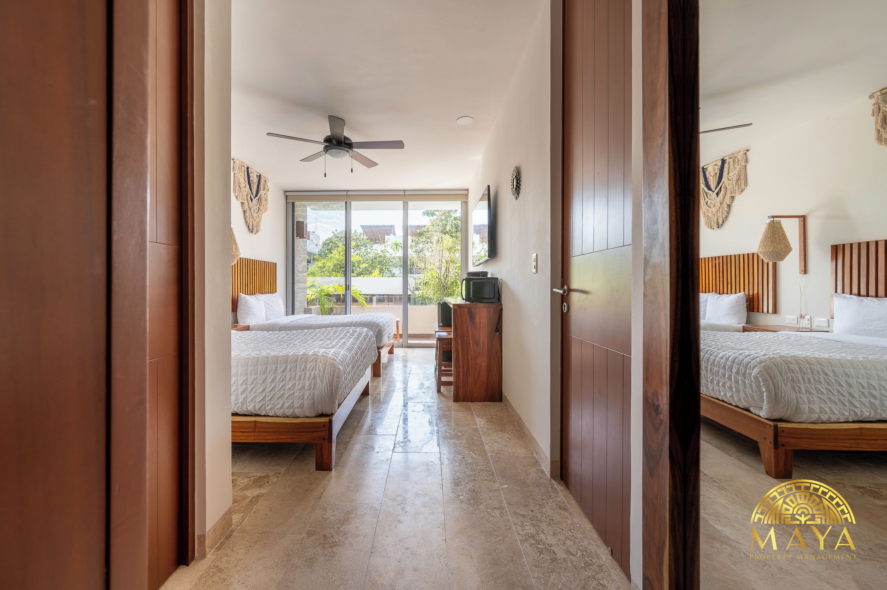 Habitación de hotel con dos camas, ventilador de techo, televisor y vistas al exterior.