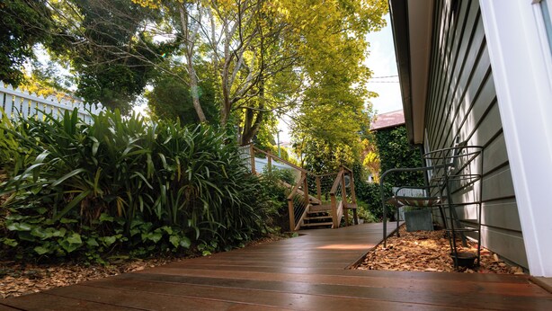 Un sendero de madera que conduce a una casa con cerca blanca y abundante vegetación.