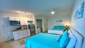 A compact hotel room with a bed, a kitchenette, and a bathroom.
