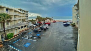 A parking lot with cars and a handicapped parking space, overlooking a beach and a building with balconies.