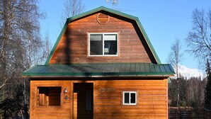 A wooden cabin with a green roof, a welcoming sign, and a window. - The Denali View Cabin (Trapper Creek)