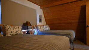 A bedroom with two beds, a wooden ceiling, a window with blinds, and a nightstand with a lamp. - The Denali View Cabin (Trapper Creek)