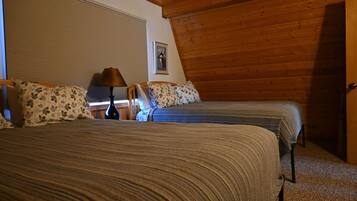 A bedroom with two beds, a wooden ceiling, a window with blinds, and a nightstand with a lamp.