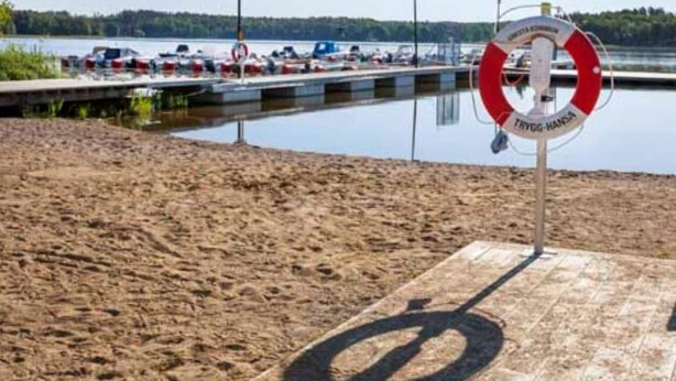 A lifebuoy sign with the text "TRIGG-HANSEN" at a dock with boats and a sandy shore. - 4 Star Holiday Home in Gnesta (Gnesta)