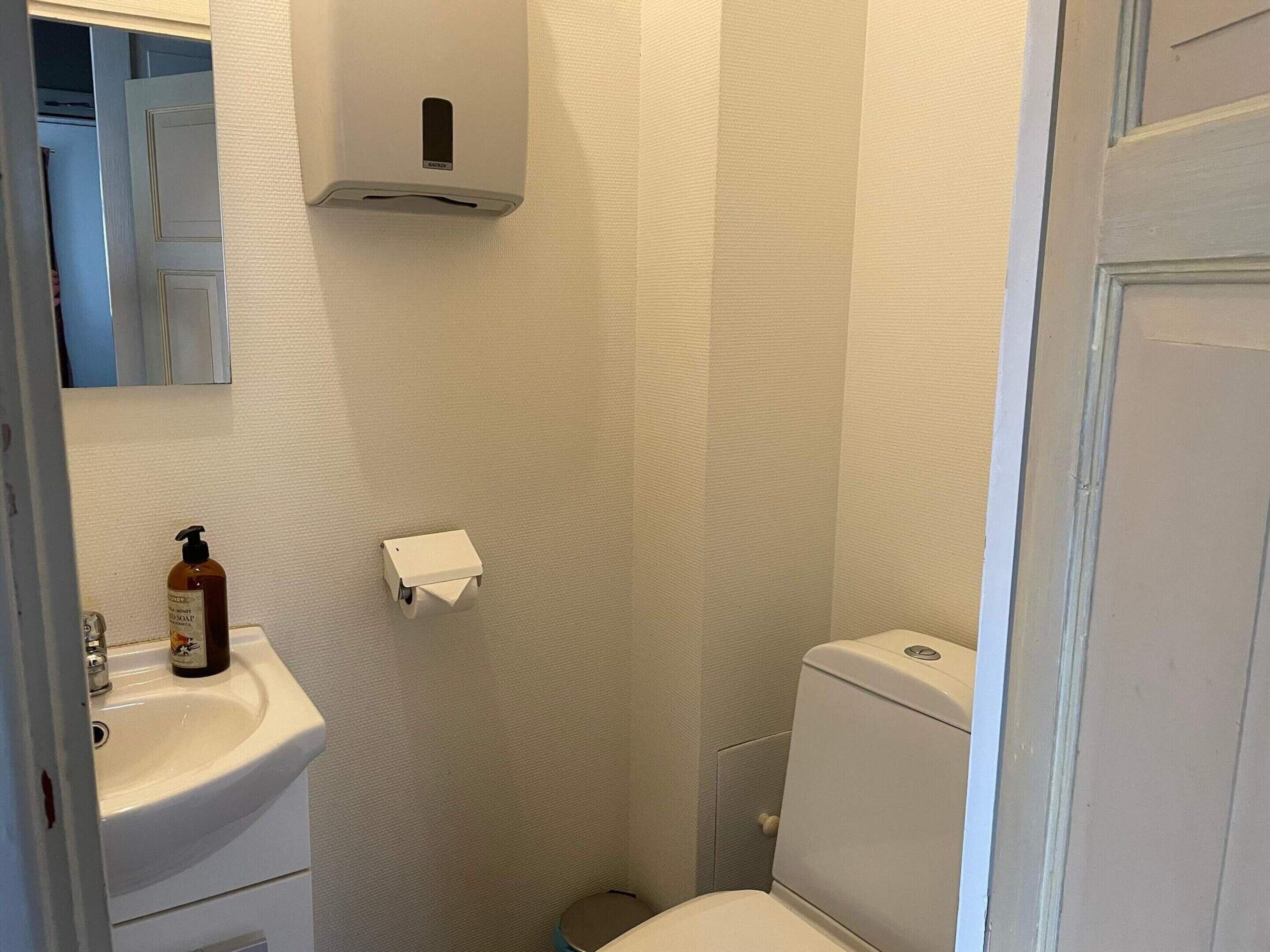A bathroom with a white sink, a toilet, and a hand soap dispenser mounted on the wall.