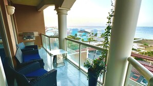 A balcony with a view of the sea, featuring a seating area with cushions and a potted plant. - Emerald of the Gulf - beachfront condo at Portofino Island resort, great views! (Pensacola Beach)