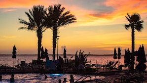 A beach scene with palm trees, lounge chairs, and umbrellas. - Emerald of the Gulf - beachfront condo at Portofino Island resort, great views! (Pensacola Beach)
