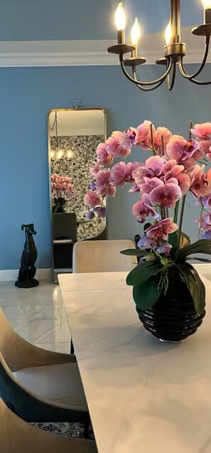 A dining area with a marble table, a vase of pink orchids, and a chandelier.