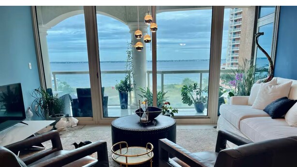 A living room with a large window overlooking the sea, a round coffee table, two armchairs, and a sofa. - Emerald of the Gulf - beachfront condo at Portofino Island resort, great views! (Pensacola Beach)